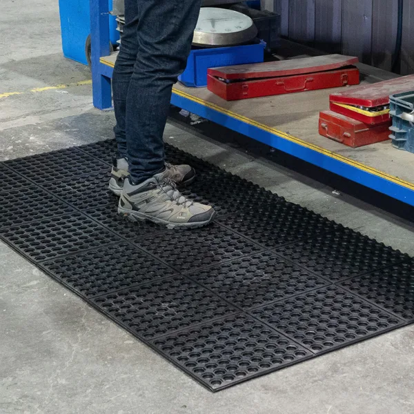 Suggested image: Person working at a garage workbench standing on rubber anti-fatigue matting. Home garage workshop with anti-fatigue rubber mat placed in front of a workbench.