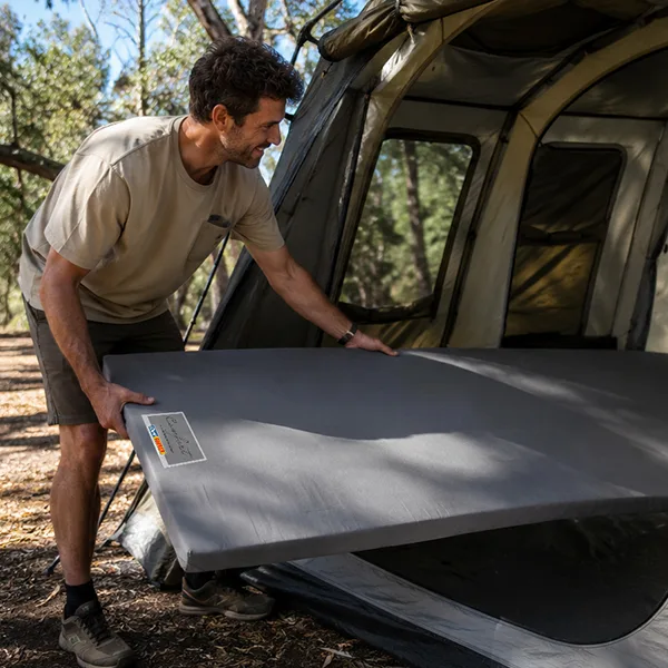 A man putting a Comfort Caravan and Camp Mattress in a tent. 