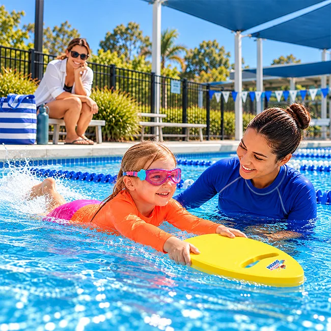 Parent actively supervising a young girl in brightly coloured sun-safe swimwear using a kickboard.